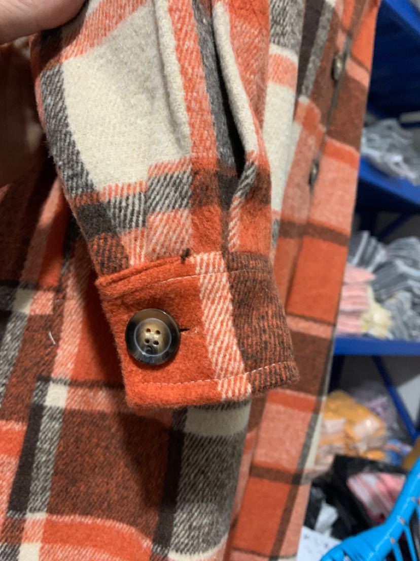 Détail manche avec bouton marron sur manteau long écossais orange en tissu tartan