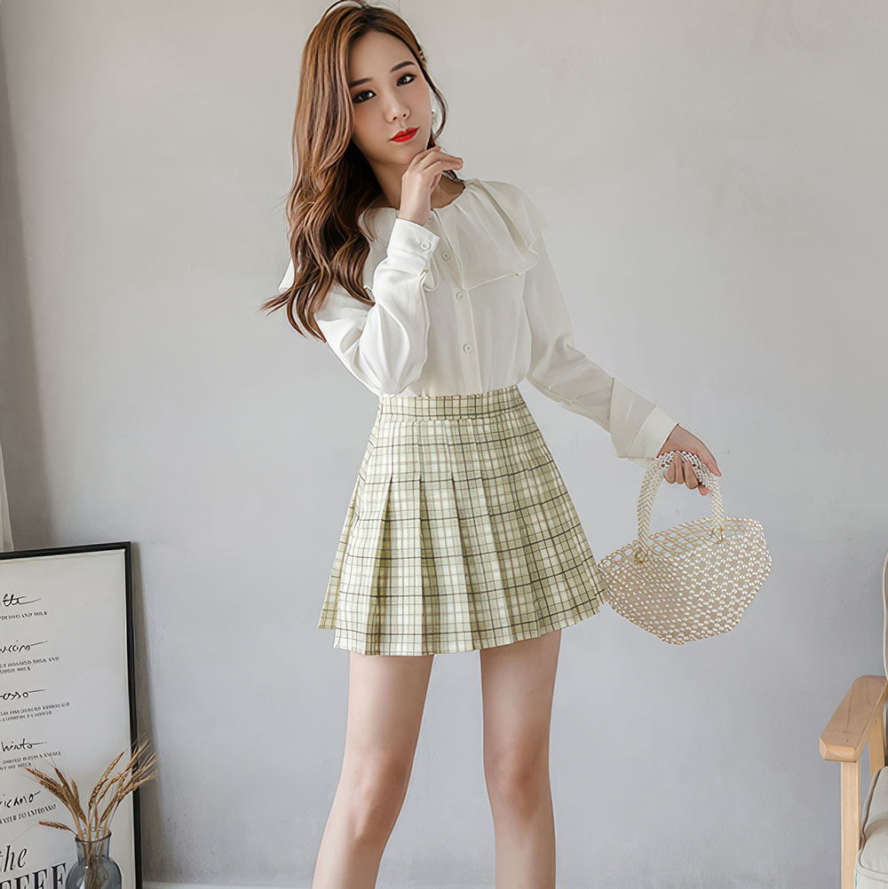 Jupe écossaise vert clair plissée en tissu tartan portée par une femme, vue de face en intérieur