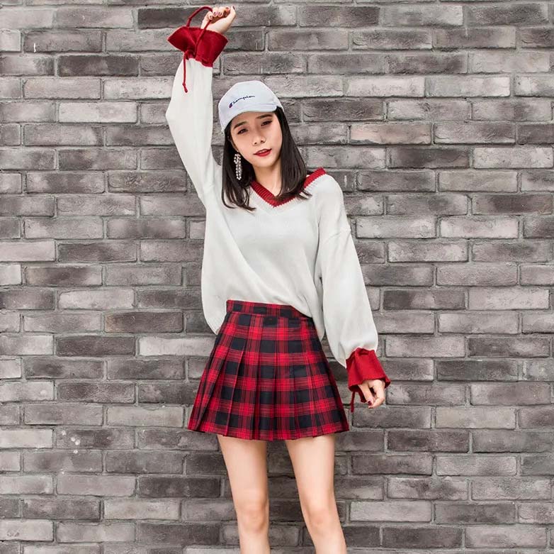 Jupe tartan rouge et noire plissée portée par une femme devant un mur en briques grises