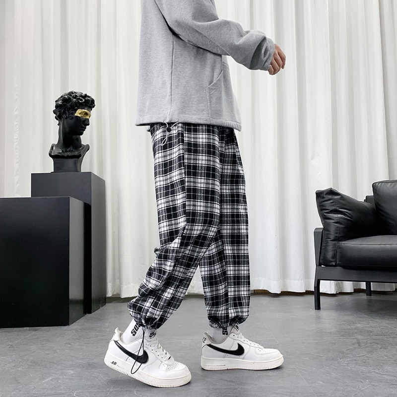 Pantalon écossais à carreaux noir et blanc porté de profil avec coupe ample et bas resserré