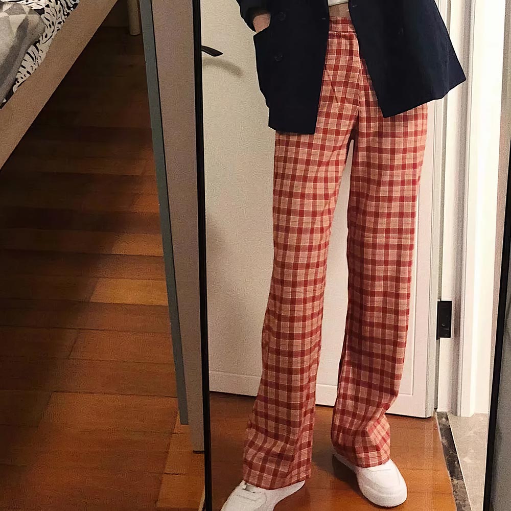 Pantalon écossais coupe droite femme en tissu tartan rouge et beige, porté avec veste noire et chaussures blanches