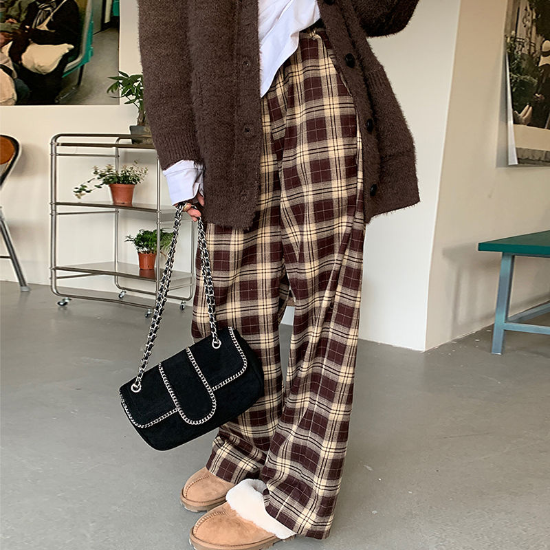 Pantalon large à carreaux écossais femme en tissu à motif tartan marron et beige porté avec un manteau marron et des chaussures beiges
