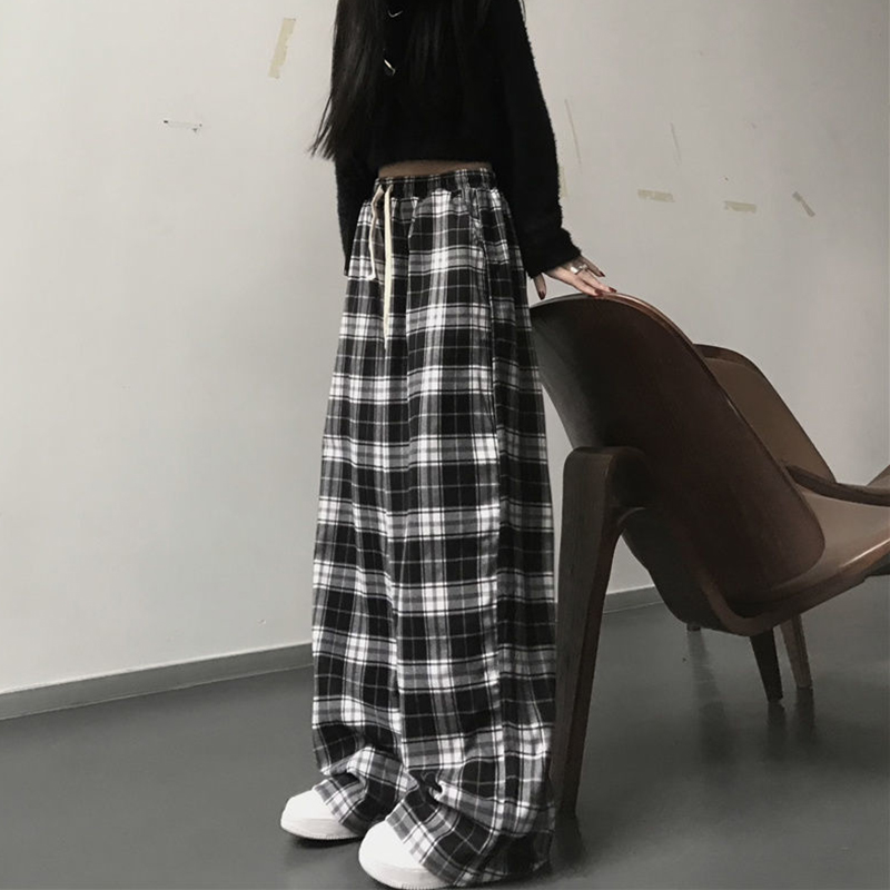 Pantalon large à carreaux écossais noir et blanc pour femme avec ceinture beige, porté avec un pull noir et des baskets blanches