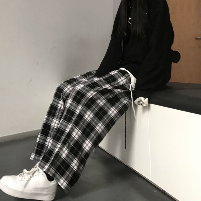 Pantalon large à carreaux écossais femme en tissu à motif tartan noir et blanc, porté assis de profil