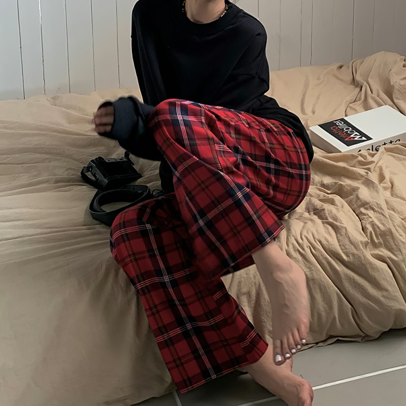 Pantalon pyjama femme rouge écossais en tissu tartan, coupe droite, porté assis sur un lit beige