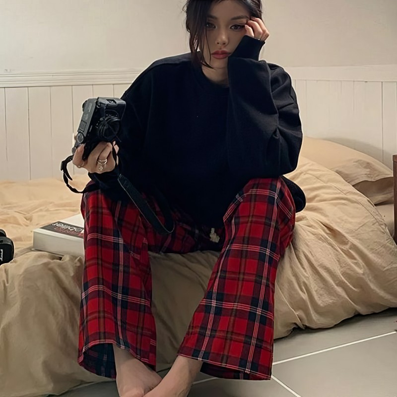 Pantalon pyjama femme rouge écossais en tissu tartan avec coupe droite, porté assise sur un lit
