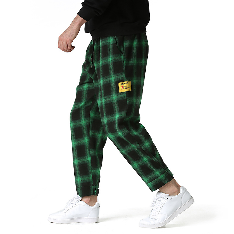 Pantalon tartan vert et noir homme en tissu à carreaux avec étiquette jaune sur la jambe, coupe décontractée et ourlets resserrés