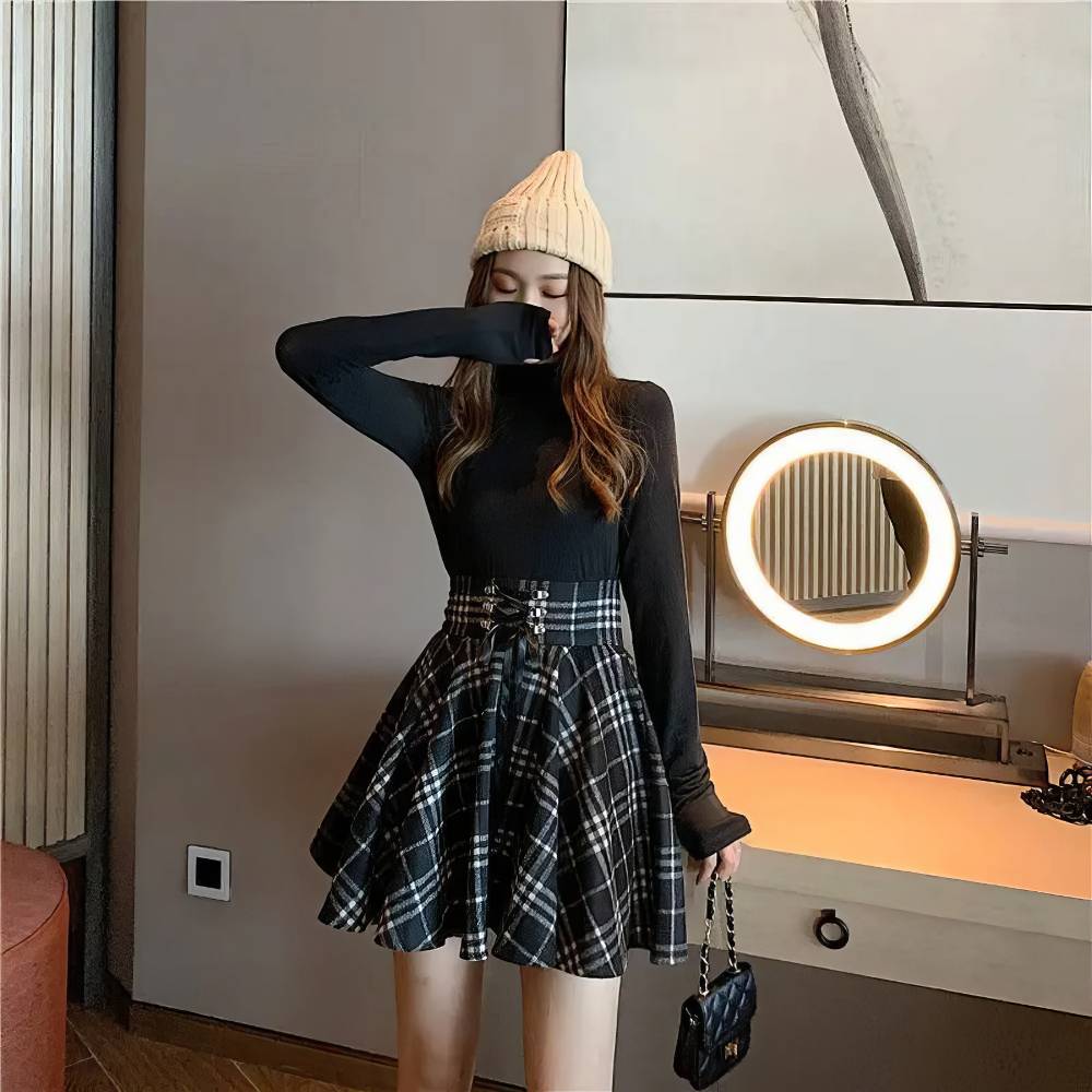 Jupe écossaise ceinture à lacets noir et blanc en tissu tartan plissé portée avec un pull noir et un bonnet beige