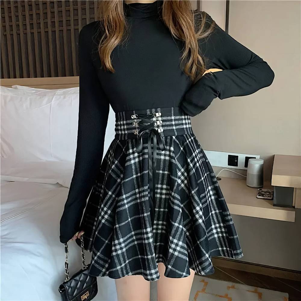 Jupe écossaise ceinture à lacets noir et blanc en tissu tartan avec taille haute et coupe évasée portée avec un haut noir à manches longues