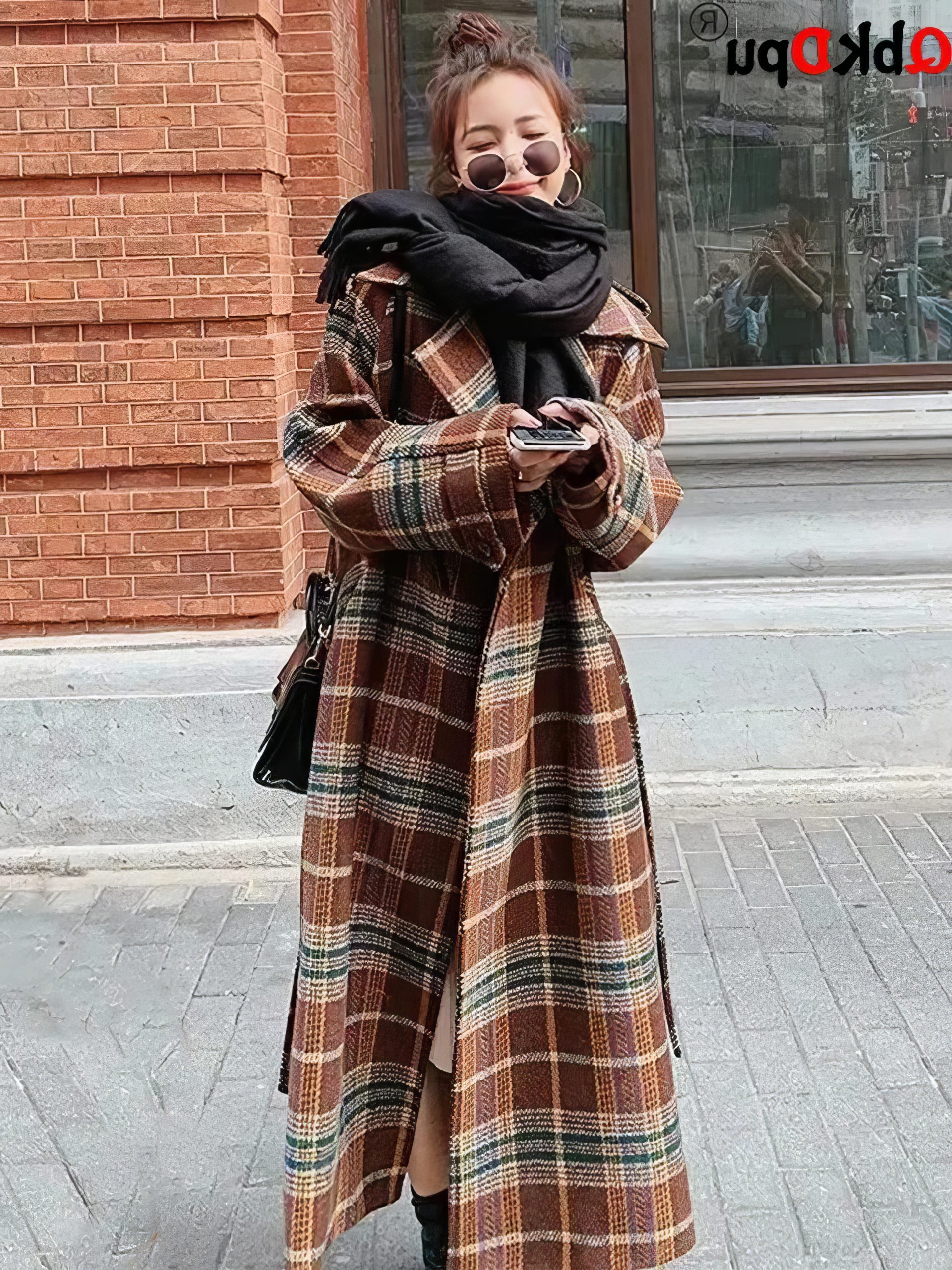 Manteau long écossais à carreaux marron et beige avec ceinture, porté par une femme en extérieur, style casual chic