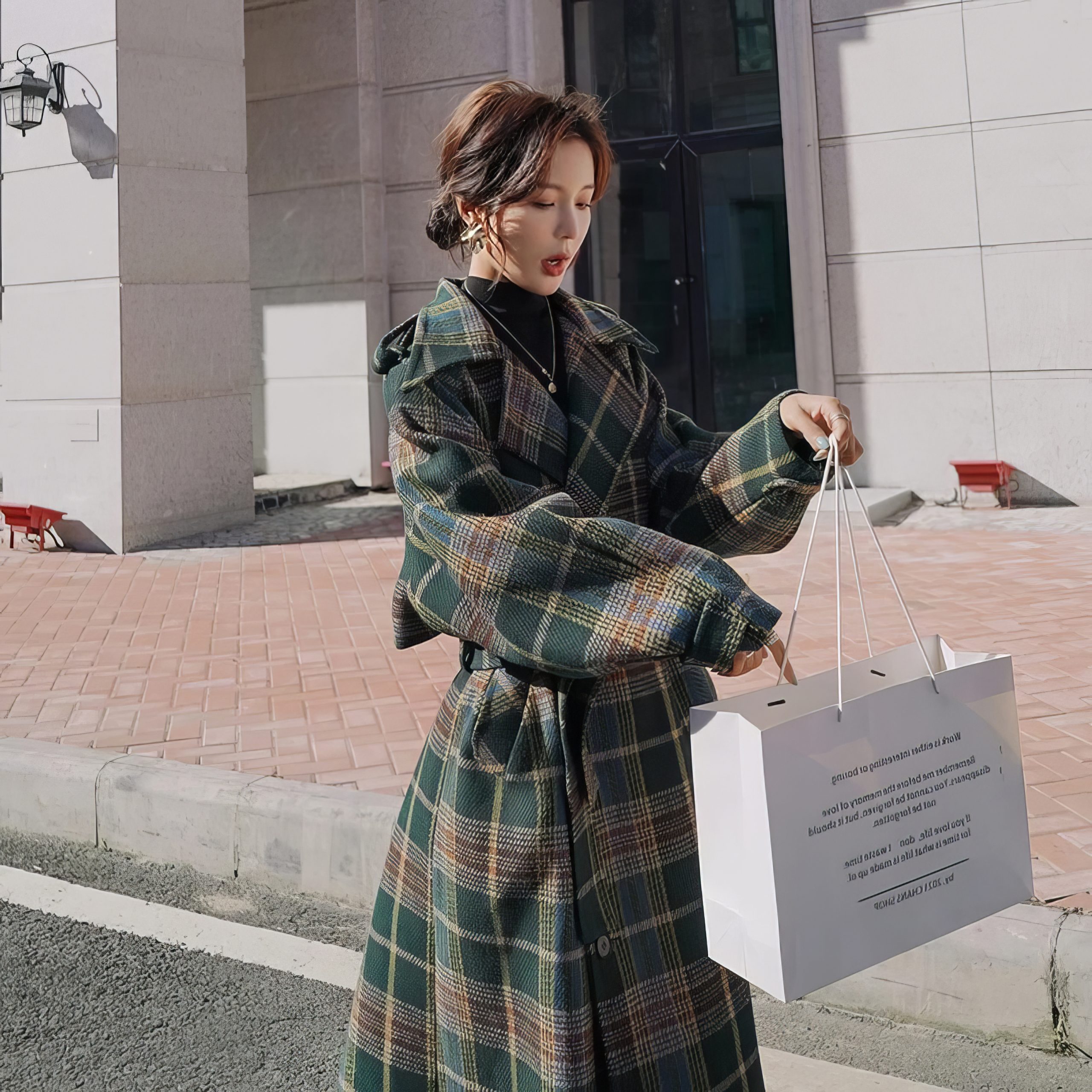 Manteau long écossais à carreaux vert et beige avec ceinture, porté par une femme en extérieur, vue de trois-quarts avec manches bouffantes