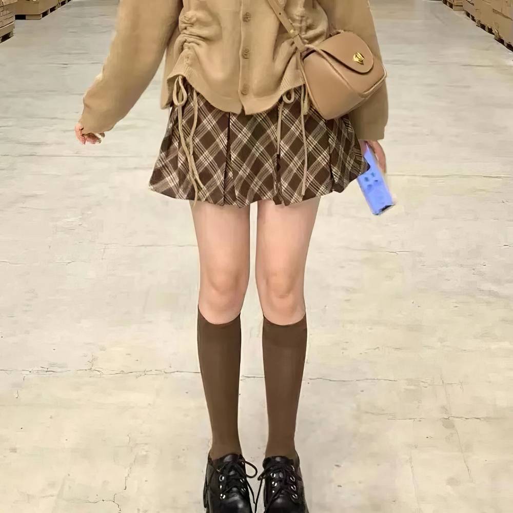 Mini jupe tartan écossaise plissée marron et beige portée avec chaussettes hautes marron et chaussures noires