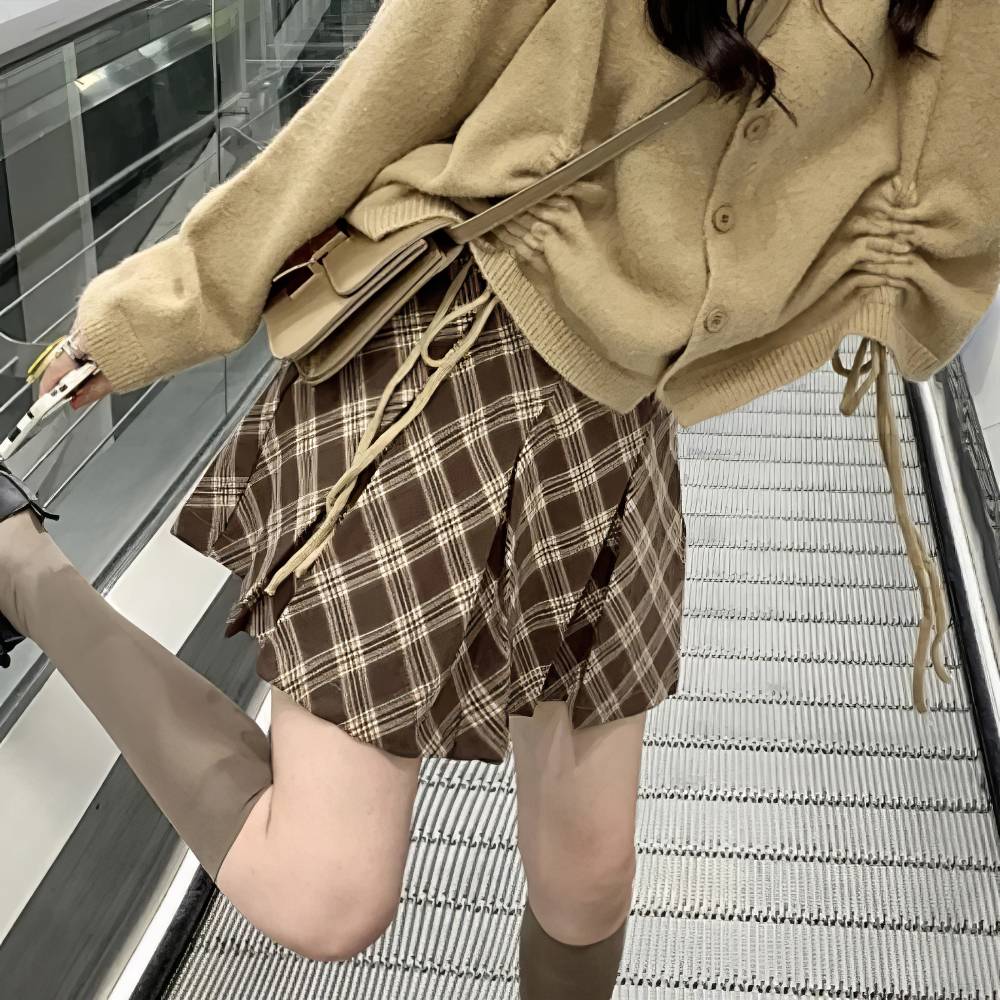 Mini jupe tartan écossaise plissée marron et beige portée vue de côté en mouvement sur escalator