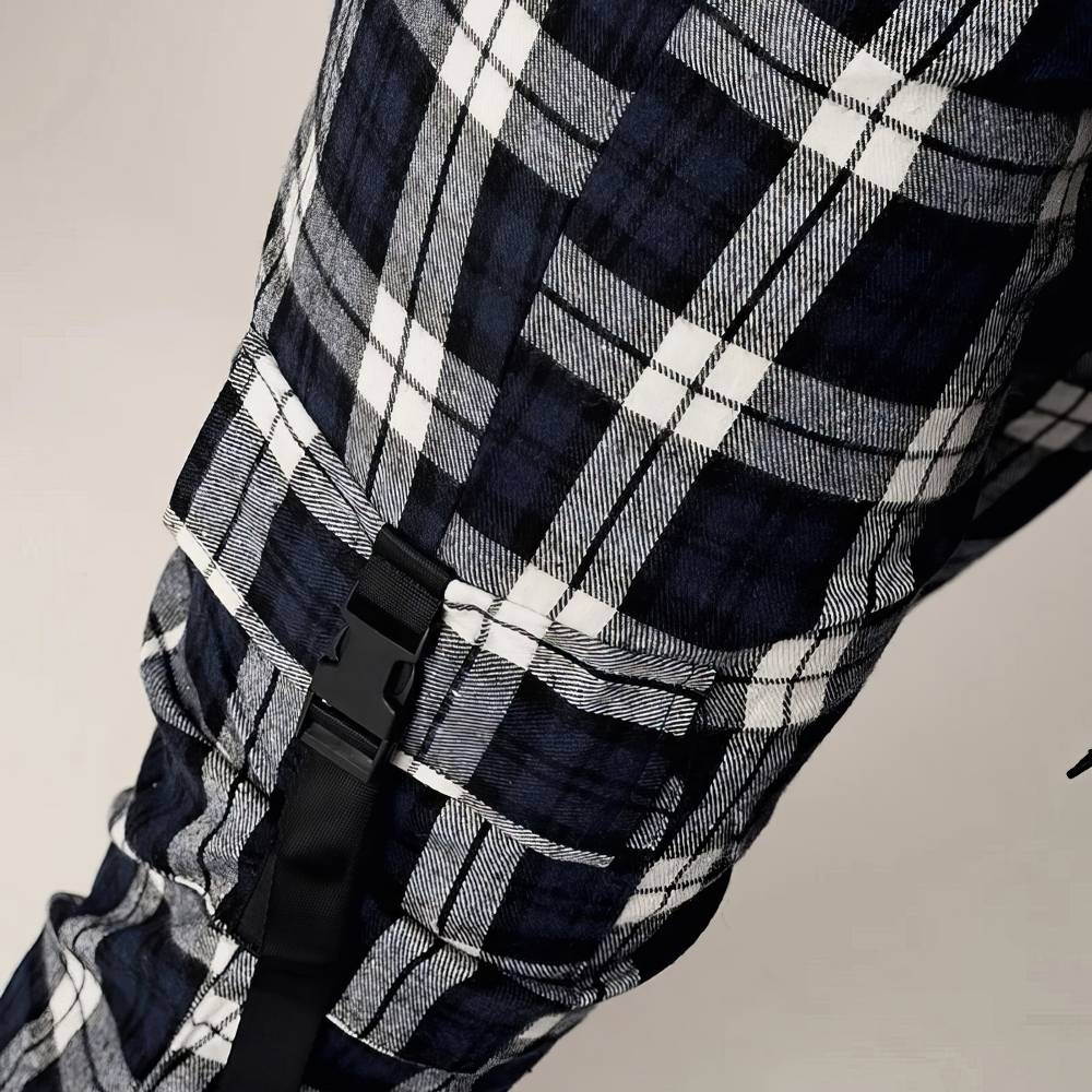 Détail du pantalon cargo écossais à carreaux noir et blanc montrant la poche latérale avec fermeture à clip et motif tartan