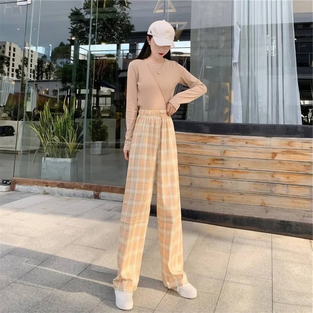 Pantalon écossais femme urbain jaune et blanc à carreaux larges, coupe droite et taille haute, porté avec un pull beige et une casquette blanche
