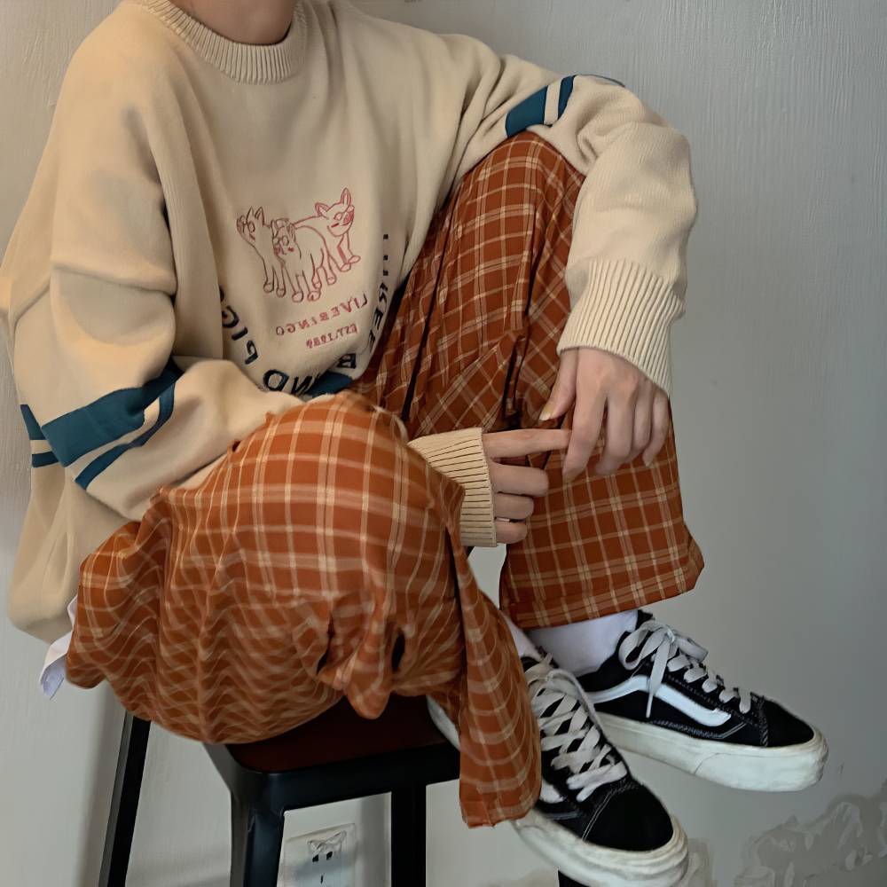 Pantalon écossais large femme orange et beige en tissu tartan, vue assise sur un tabouret avec sweat beige et baskets noires