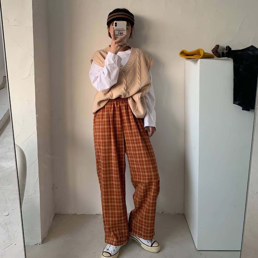 Pantalon écossais large femme orange et beige en tissu tartan, coupe droite, porté avec un pull beige et un t-shirt blanc