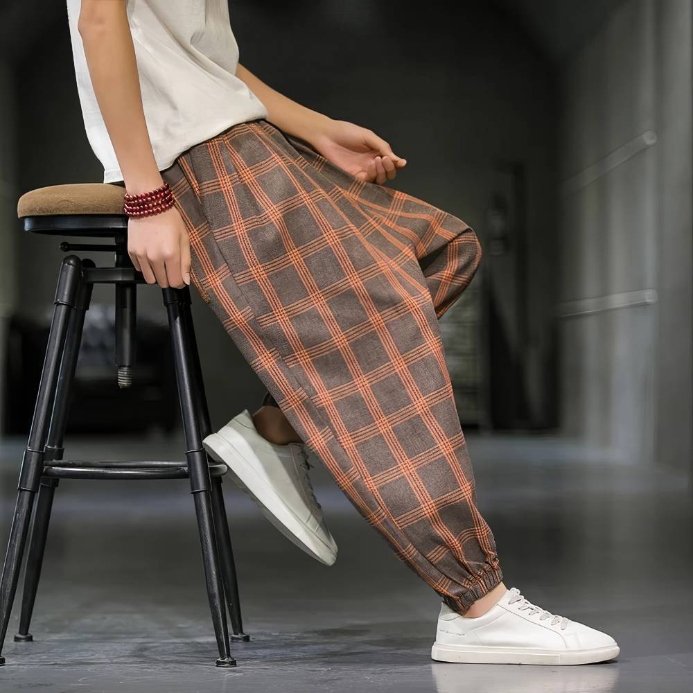 Pantalon écossais homme large marron et orange en tissu tartan avec coupe ample et bas resserré, porté assis de profil