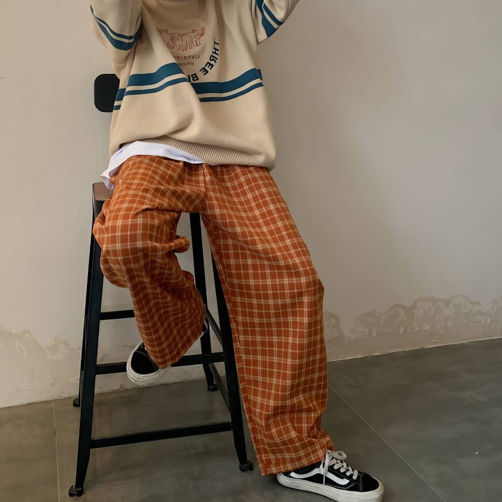 Pantalon large femme orange et beige à motif écossais tartan, porté assis sur un tabouret, style casual chic