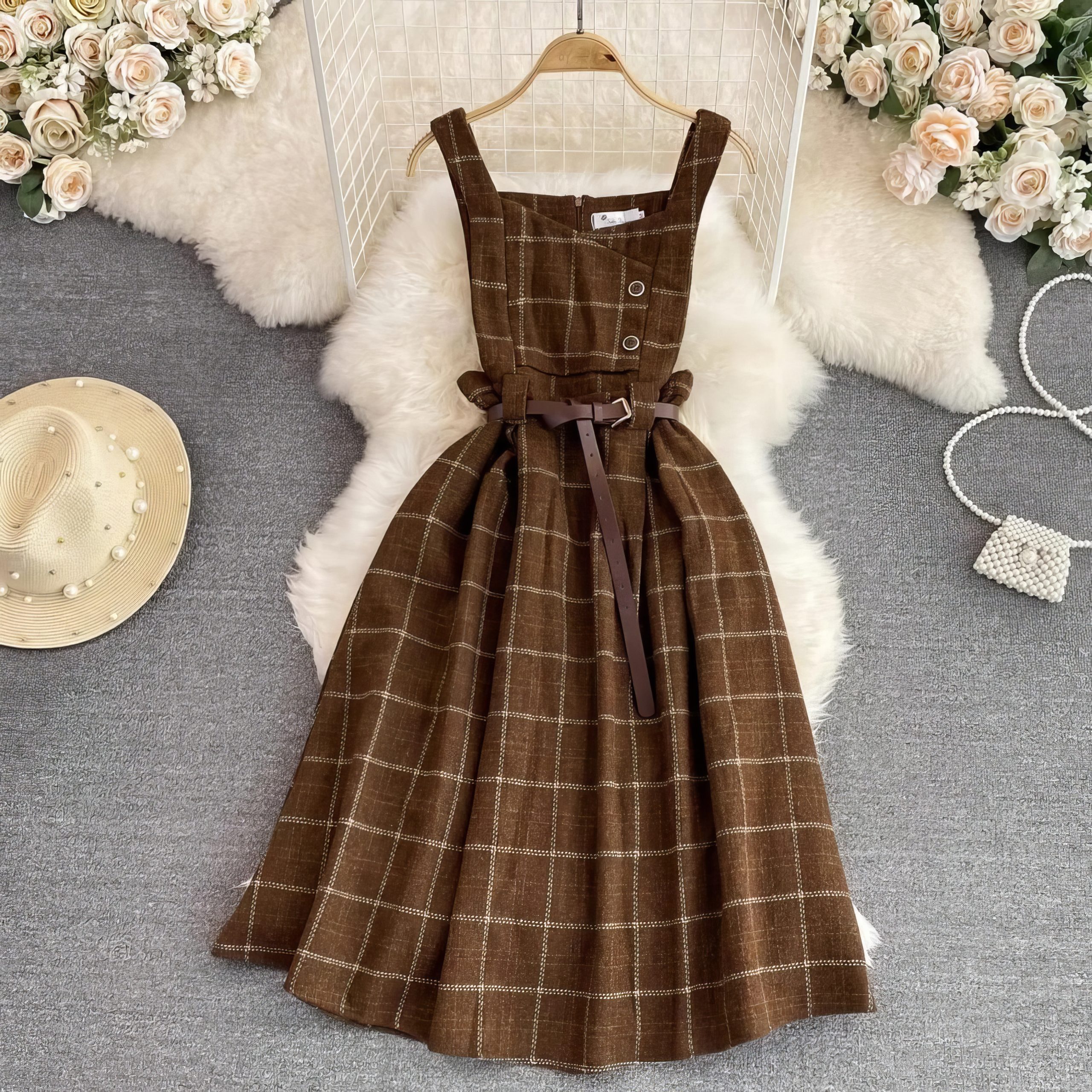 Robe écossaise chasuble marron en tissu à carreaux avec ceinture marron, vue de face posée sur un tapis gris avec décor floral