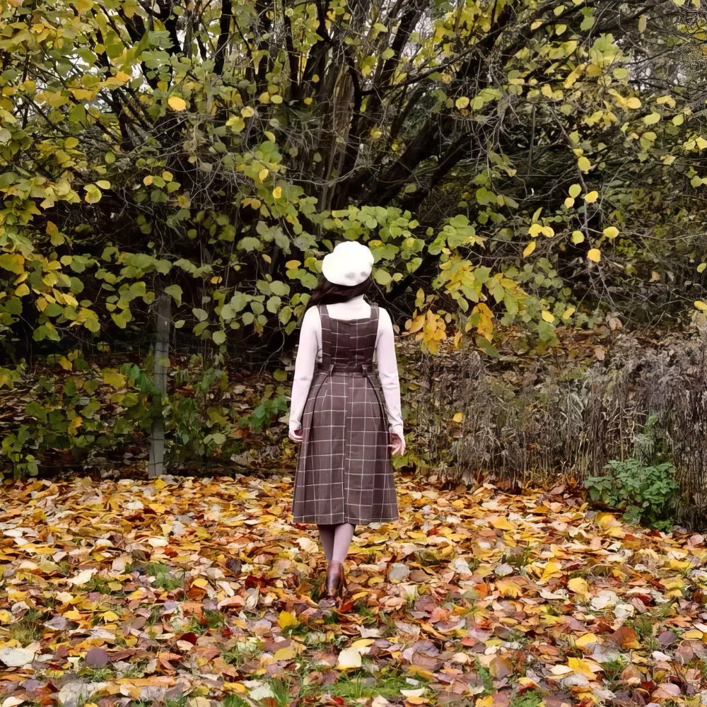 Femme de dos portant une robe écossaise chasuble marron à motif tartan avec ceinture, en automne dans un parc aux feuilles mortes