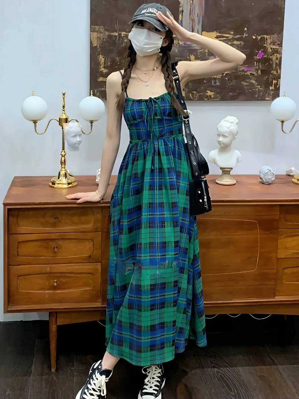 Robe écossaise longue à bretelles fines en motif tartan vert et bleu portée en intérieur avec chaussures noires et blanches